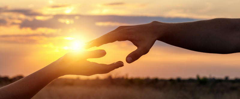 Zwei Hände berühren sich vor einem Sonnenuntergang